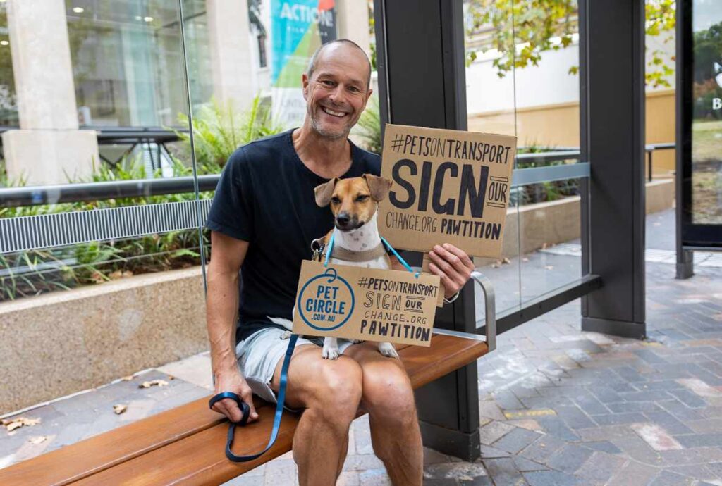 Jon Wild at bus shelter with his dog and Pet Circle petition for pets on public transport 